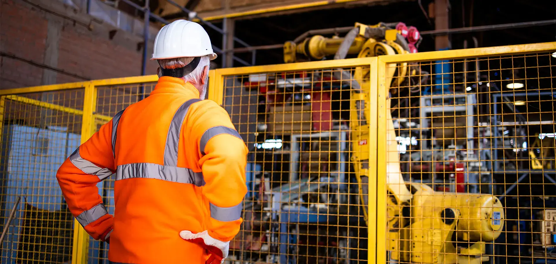 Factory worker in safety uniform controlling operation of industrial robotic arm in production department.